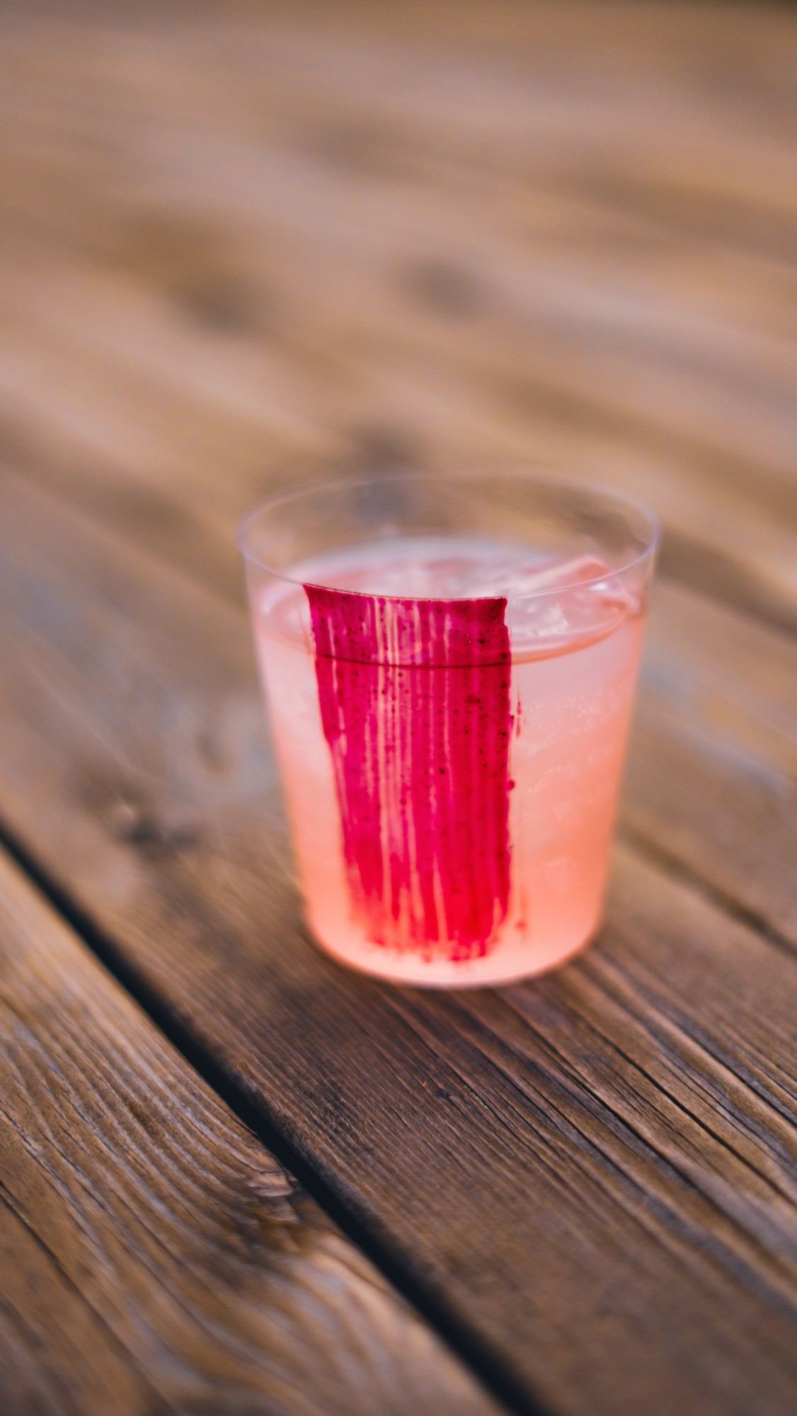 Glass med rosa drink og et strøk rød PAINTZ på utsiden, på et trebord